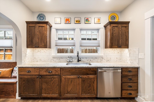 kitchen with a sink, decorative backsplash, light stone counters, and stainless steel dishwasher