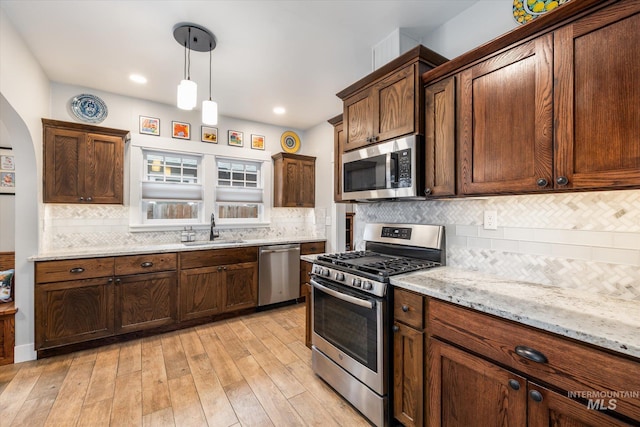 kitchen with a sink, stainless steel appliances, light wood-style floors, decorative backsplash, and hanging light fixtures