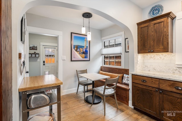 dining space with arched walkways, light wood-style flooring, breakfast area, and baseboards