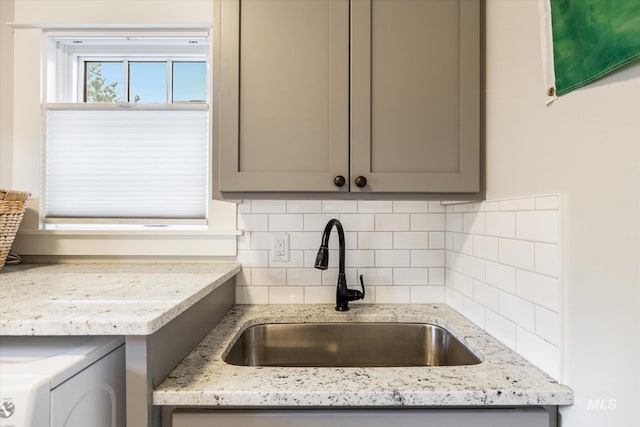 kitchen featuring washer / dryer, gray cabinets, tasteful backsplash, and a sink