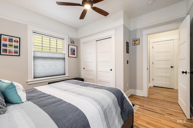 bedroom featuring light wood finished floors, ceiling fan, baseboards, and a closet