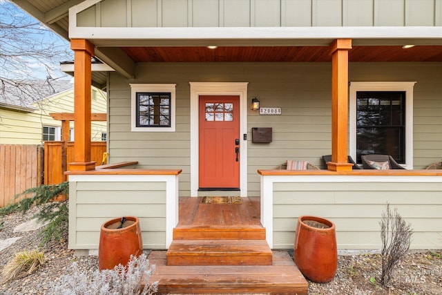 doorway to property featuring covered porch, fence, and board and batten siding