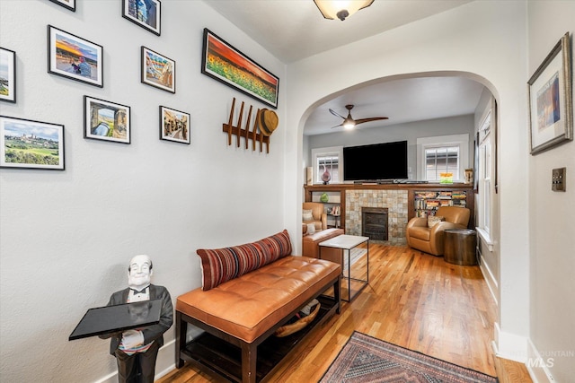 living room with baseboards, light wood finished floors, a fireplace, arched walkways, and ceiling fan