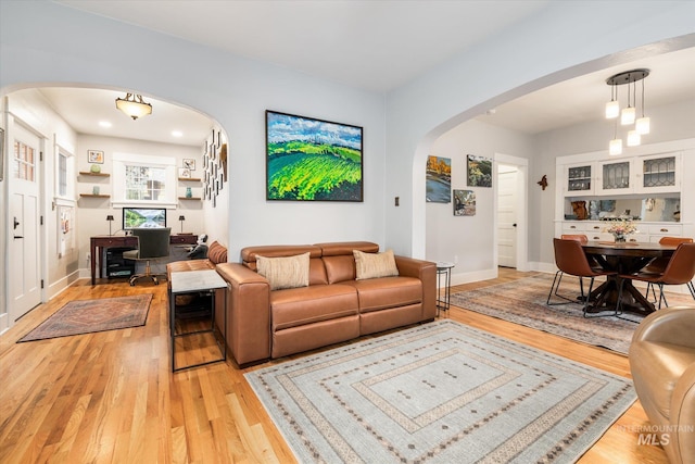 living area with light wood-style floors, arched walkways, and baseboards