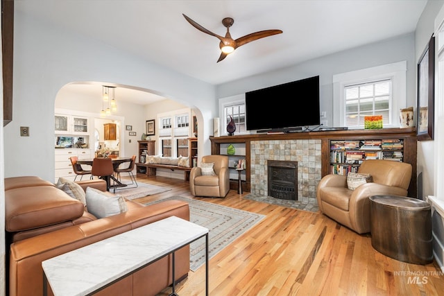 living area featuring arched walkways, light wood-style floors, ceiling fan, and a tile fireplace