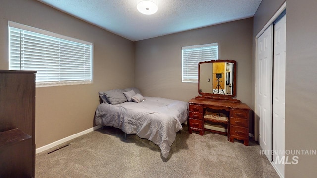 bedroom with a textured ceiling, light carpet, visible vents, baseboards, and a closet