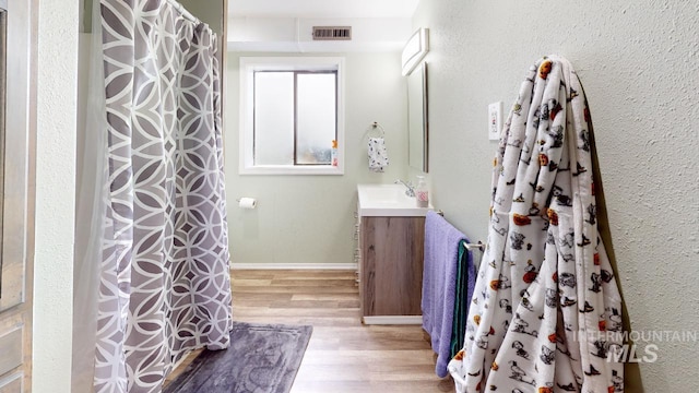 full bath with visible vents, a shower with shower curtain, vanity, wood finished floors, and baseboards