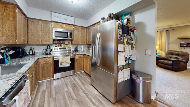 kitchen with stainless steel appliances, open floor plan, brown cabinetry, and light stone countertops