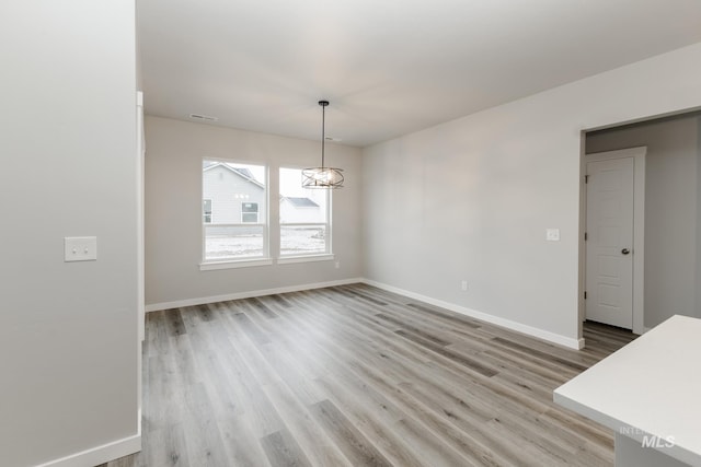 unfurnished dining area featuring baseboards, light wood-type flooring, and a chandelier