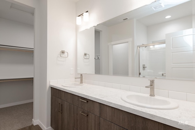 bathroom with double vanity, a spacious closet, a stall shower, and a sink