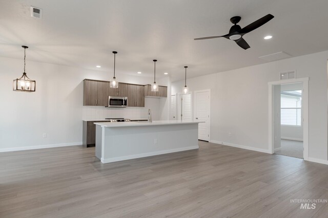 kitchen featuring stainless steel microwave, backsplash, visible vents, open floor plan, and light wood-type flooring