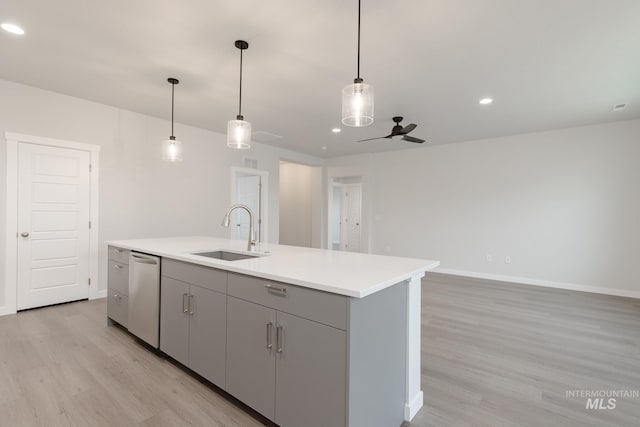 kitchen featuring light wood finished floors, a kitchen island with sink, a sink, hanging light fixtures, and dishwasher