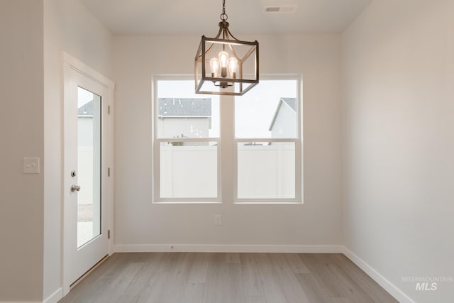 unfurnished dining area with visible vents, plenty of natural light, light wood-type flooring, and an inviting chandelier