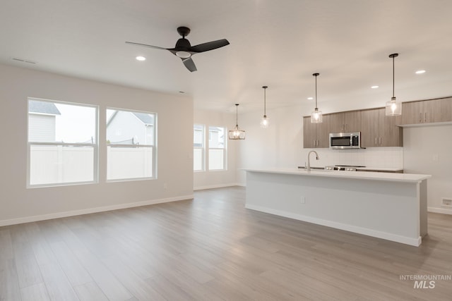 kitchen featuring a ceiling fan, light countertops, light wood-style floors, stainless steel microwave, and tasteful backsplash