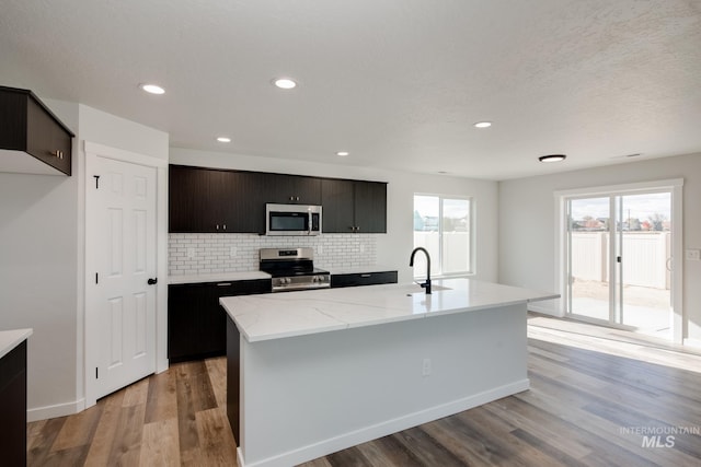 kitchen featuring light wood-type flooring, a kitchen island with sink, stainless steel appliances, and light countertops