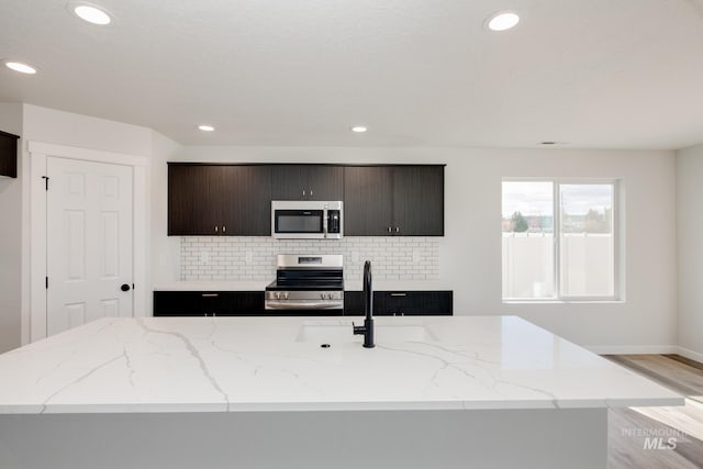 kitchen with appliances with stainless steel finishes, a sink, light stone counters, and tasteful backsplash