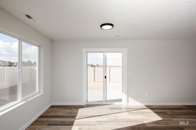 empty room featuring visible vents, a textured ceiling, baseboards, and dark wood-style flooring