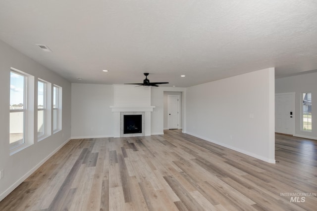 unfurnished living room featuring light wood finished floors, a fireplace, baseboards, and a textured ceiling