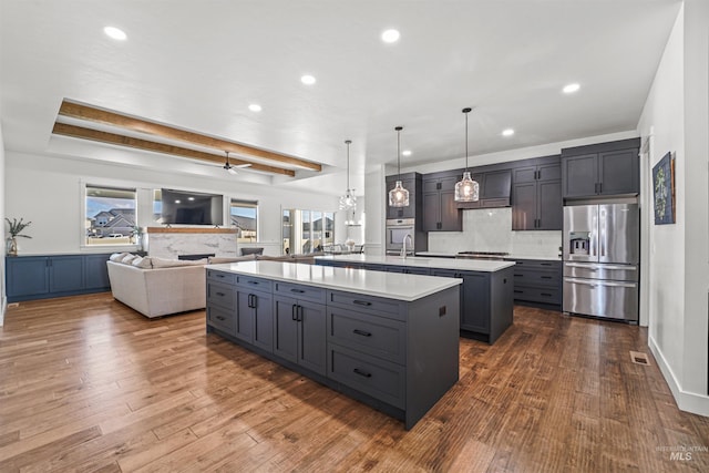 kitchen with light countertops, stainless steel fridge, dark wood-type flooring, open floor plan, and a center island