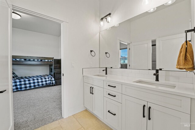 ensuite bathroom with double vanity, connected bathroom, backsplash, and a sink