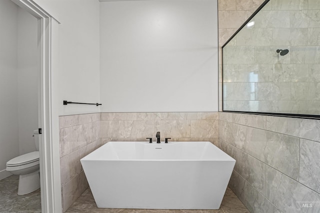 full bath featuring a freestanding bath, toilet, and tile walls