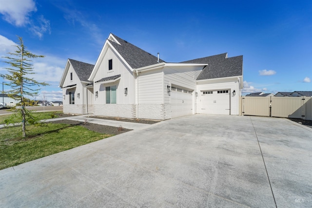 view of side of property with board and batten siding, a shingled roof, concrete driveway, an attached garage, and a gate