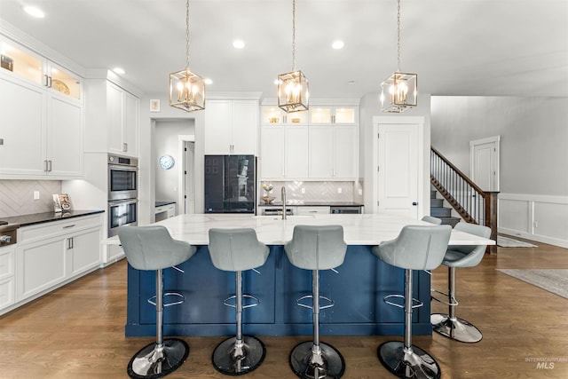 kitchen featuring stainless steel double oven, white cabinets, hanging light fixtures, and black fridge