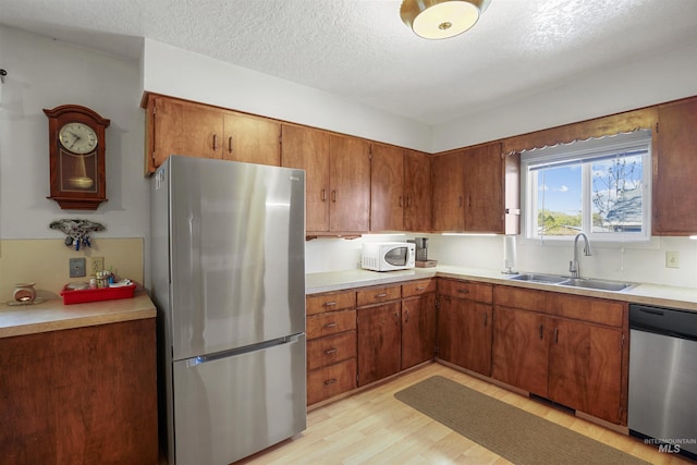kitchen with a sink, stainless steel appliances, brown cabinetry, light wood-type flooring, and light countertops