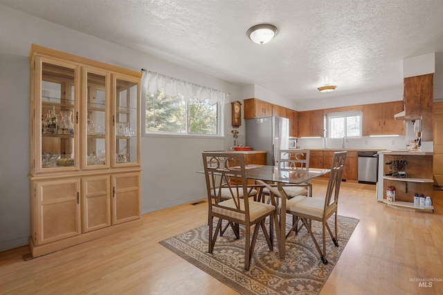 dining room featuring a textured ceiling, baseboards, and light wood-type flooring