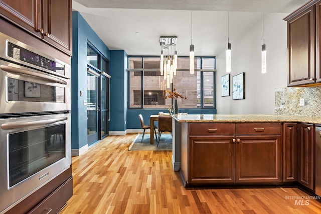 kitchen featuring hanging light fixtures, double oven, tasteful backsplash, and light wood-type flooring