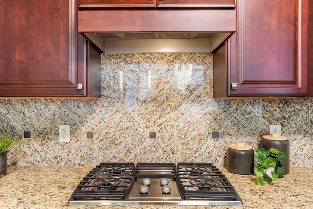 kitchen with light stone counters, stainless steel gas stovetop, dark brown cabinets, under cabinet range hood, and backsplash