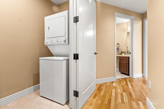 washroom with light wood-style flooring, baseboards, and stacked washer / drying machine