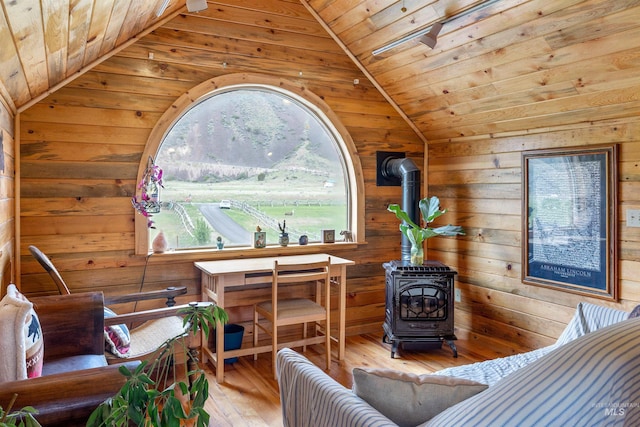 living room with light wood-type flooring, wood ceiling, a wood stove, wooden walls, and lofted ceiling