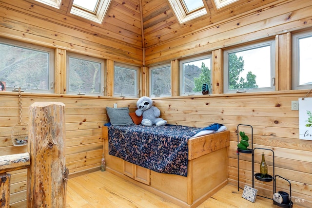 bedroom with wooden walls, light hardwood / wood-style flooring, vaulted ceiling with skylight, and wooden ceiling