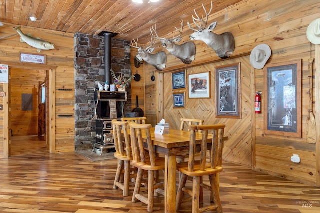 dining area featuring wood-type flooring, wooden walls, a wood stove, and wooden ceiling