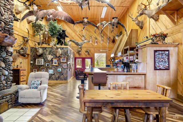 dining area with high vaulted ceiling, wooden ceiling, wooden walls, and wood-type flooring