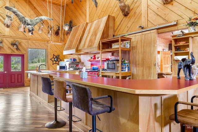 kitchen with hanging light fixtures, high vaulted ceiling, wood-type flooring, sink, and wooden walls