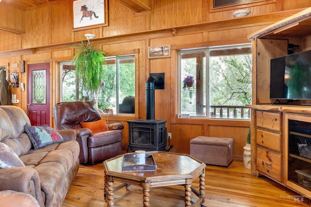 living room featuring light hardwood / wood-style floors, plenty of natural light, wooden walls, and a wood stove