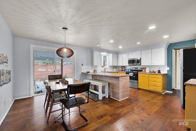 kitchen featuring kitchen peninsula, appliances with stainless steel finishes, dark hardwood / wood-style flooring, white cabinetry, and hanging light fixtures