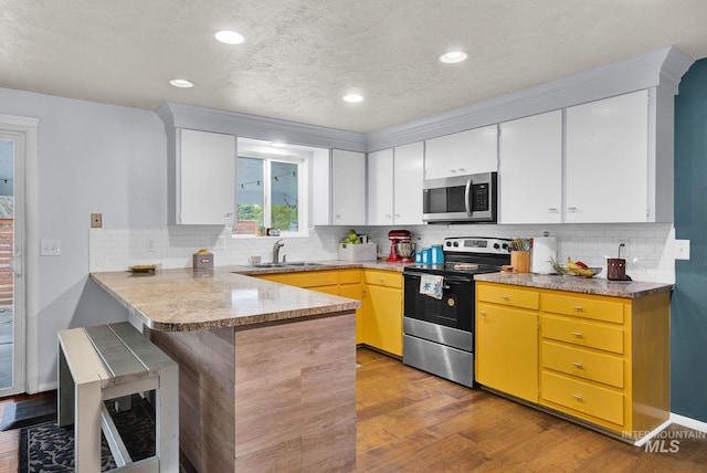 kitchen with sink, stainless steel appliances, kitchen peninsula, white cabinets, and light wood-type flooring