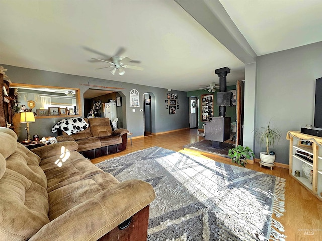 living room featuring a wood stove, arched walkways, a ceiling fan, and wood finished floors