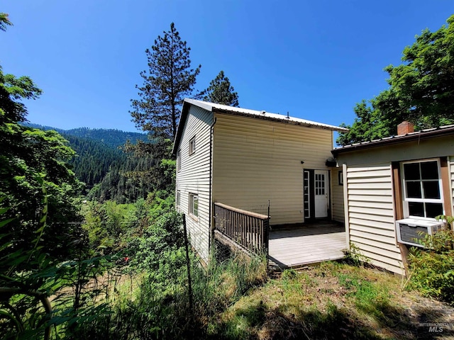 back of property with a chimney, a deck, cooling unit, and a forest view