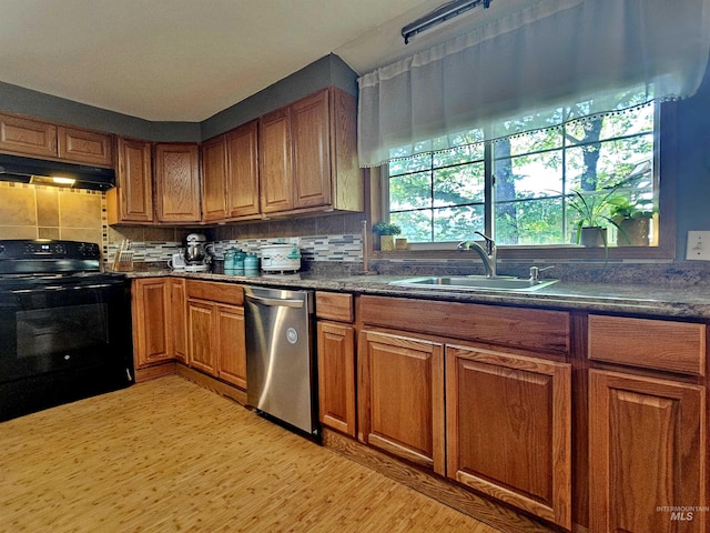 kitchen featuring under cabinet range hood, dishwasher, brown cabinetry, a sink, and black range with electric cooktop