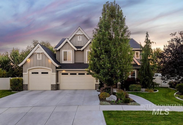 craftsman house with board and batten siding, driveway, a yard, an attached garage, and stone siding