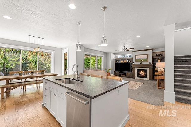 kitchen featuring white cabinets, a sink, light wood-style floors, stainless steel dishwasher, and a lit fireplace