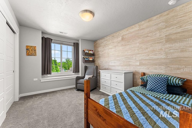 carpeted bedroom featuring wooden walls, baseboards, a textured ceiling, and visible vents