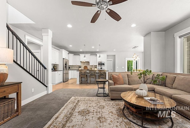 living room with ceiling fan, light colored carpet, recessed lighting, baseboards, and stairway