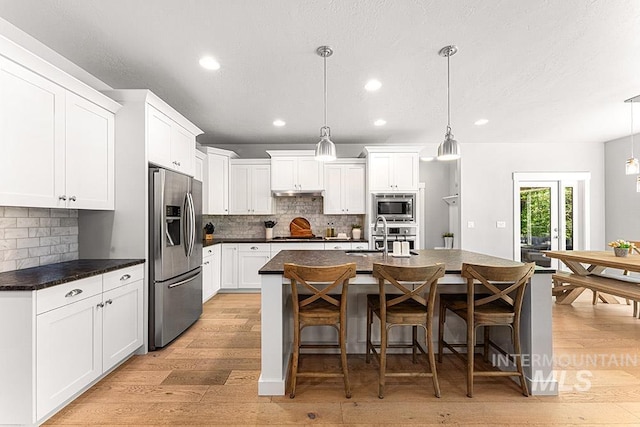 kitchen featuring dark countertops, backsplash, stainless steel appliances, and light wood finished floors