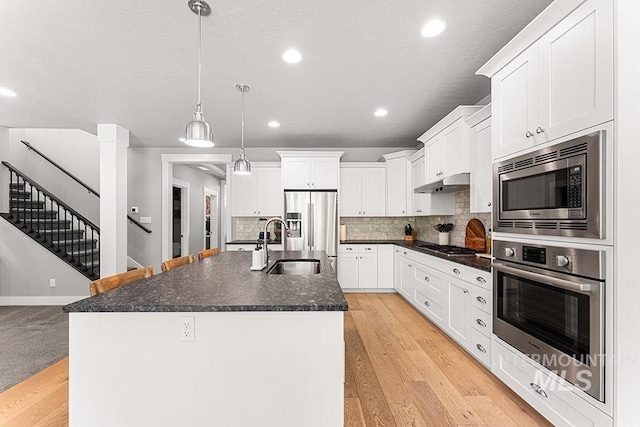 kitchen featuring decorative backsplash, stainless steel appliances, a sink, under cabinet range hood, and an island with sink