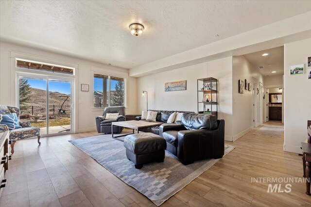 living area featuring recessed lighting, light wood-style floors, baseboards, and a textured ceiling